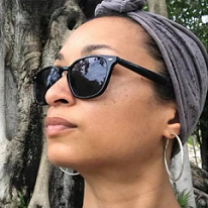 Young black woman with a scarf on her head and sunglasses looking left in front of a tree