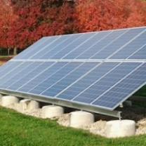 Big silver solar panel on ground sideways aimed at sky with red leaved trees in the background