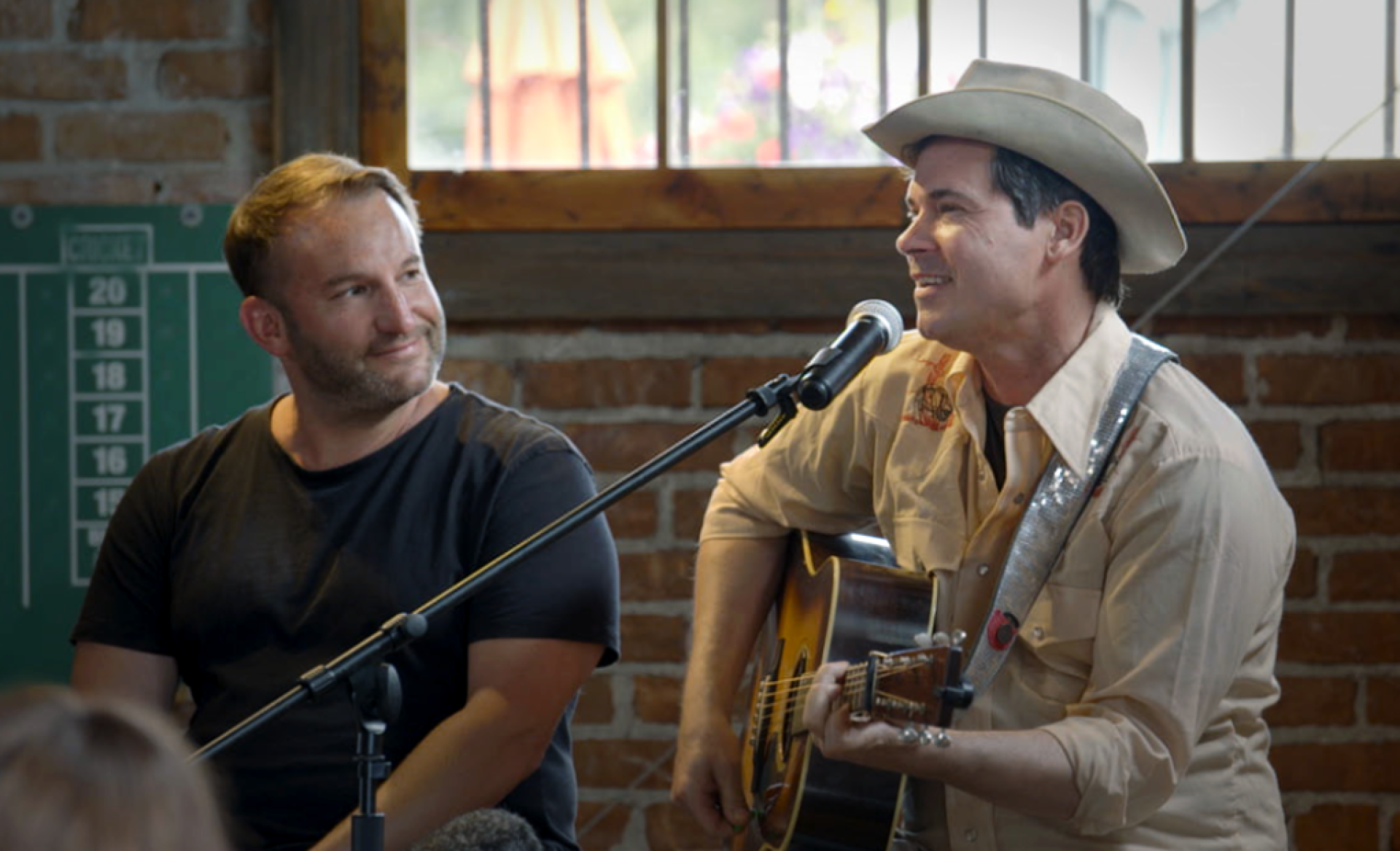 Two white guys talking one with a guitar