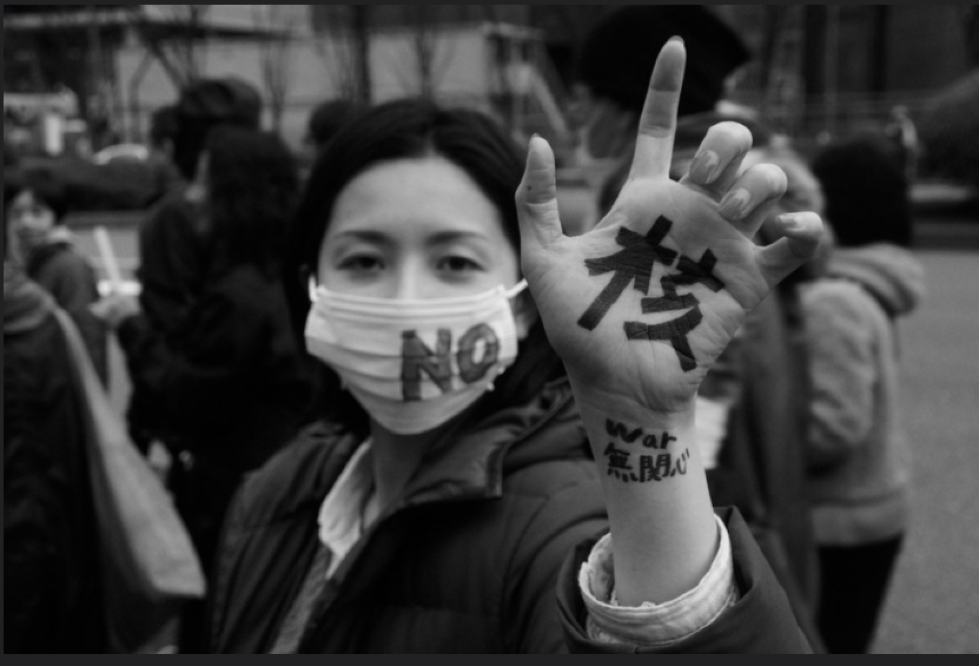 Young Japanese woman with mask on that says No and her hand says Nukes in Japanese